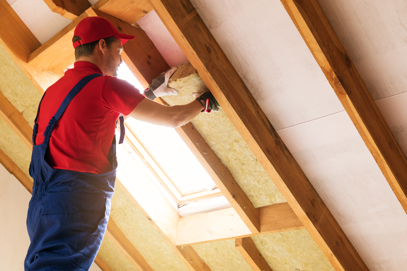 image of a man dressed in overalls and a red t-shirt insulating the roof of the house