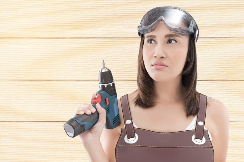A woman wearing overalls and goggles while holding a drill