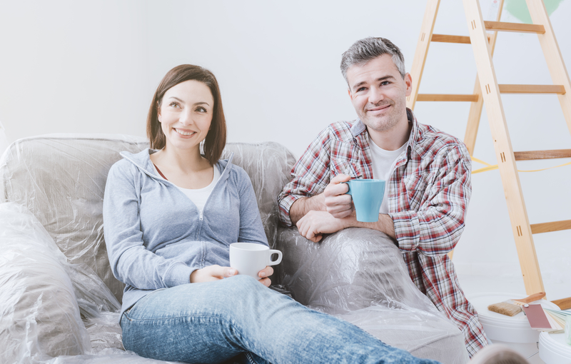 A couple sipping on coffee or tea while sitting on their couch while renovations are on going